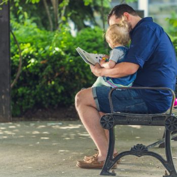 Papa liest mit Kind im Park